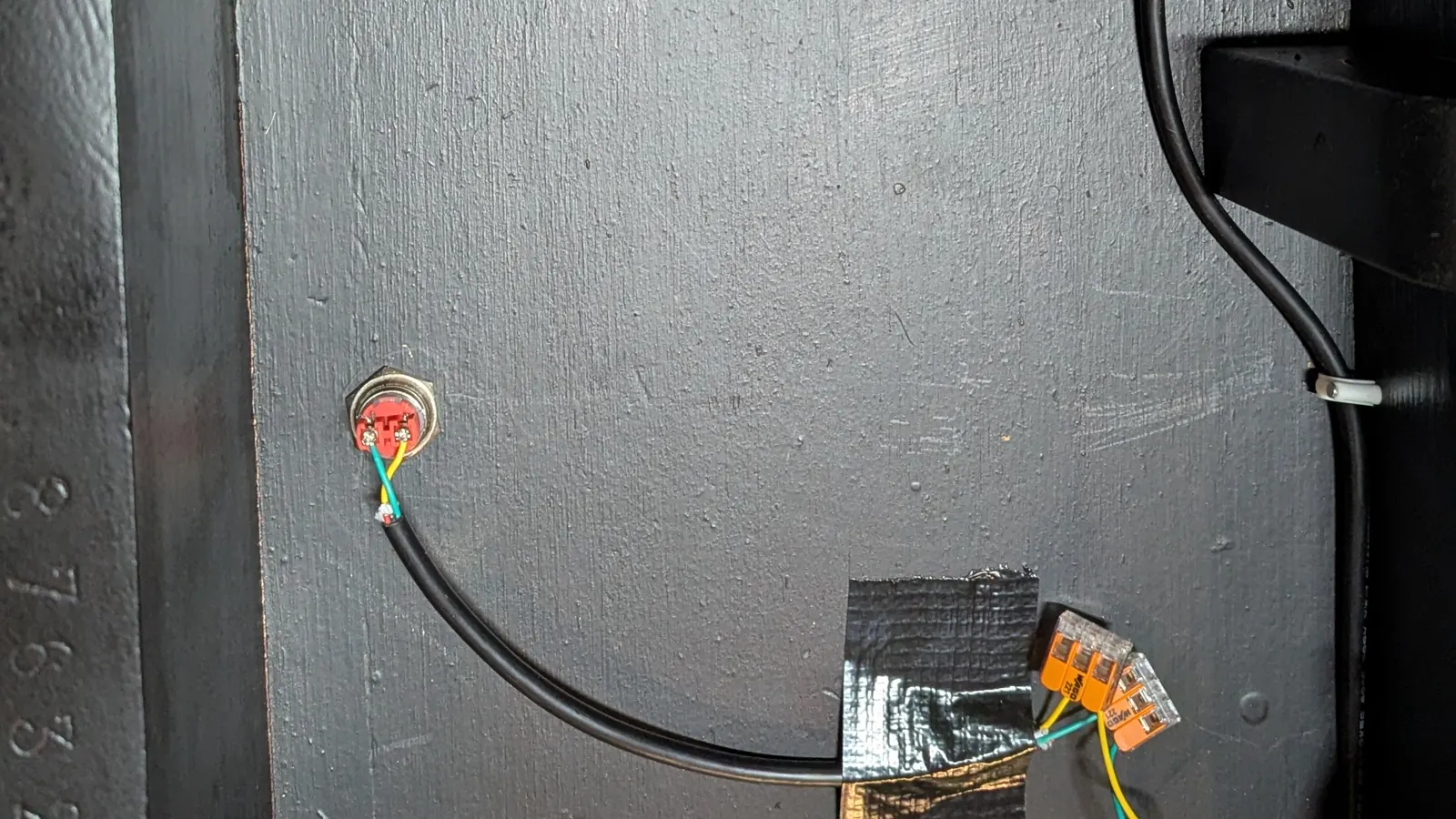 El interruptor general, un pulsador redondo con anillo rojo atornillado por debajo del mueble